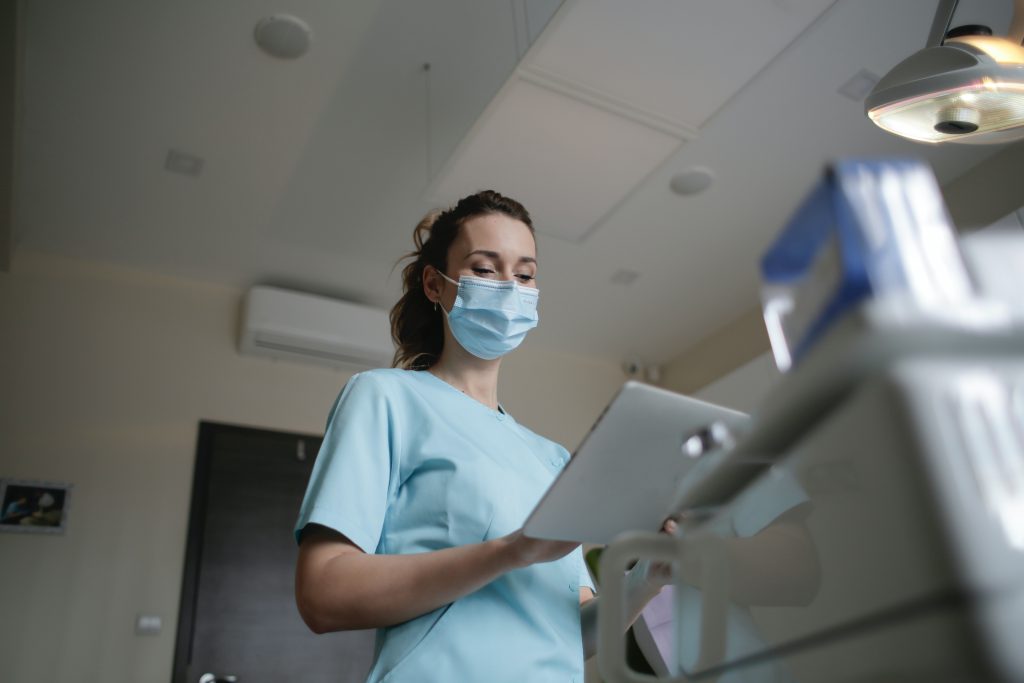 A female paramedic in a uniform and wearing a mask examines a patient's test results in a patient room inside the hospital.