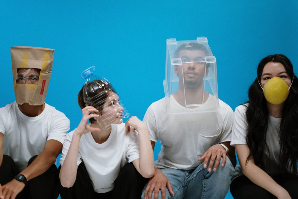 A man has McDonalds bag on his head, a woman wearing  bottle, a man with plastic box on his head, and a woman wearing mask. 