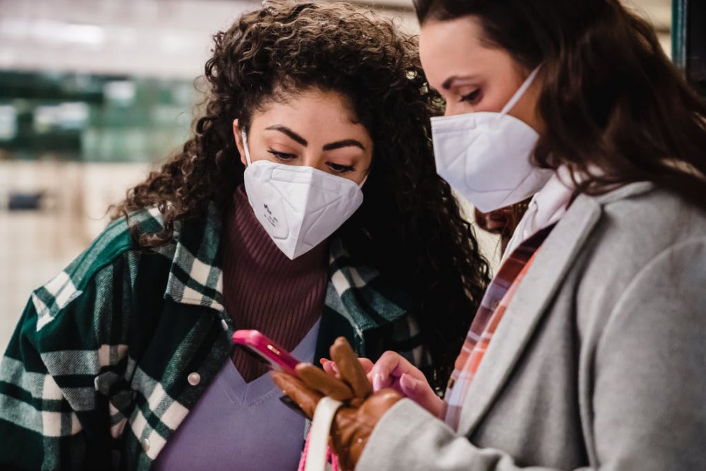 Two women wearing N95 masks are standing inside the mall and looking at the phone one of them is holding.