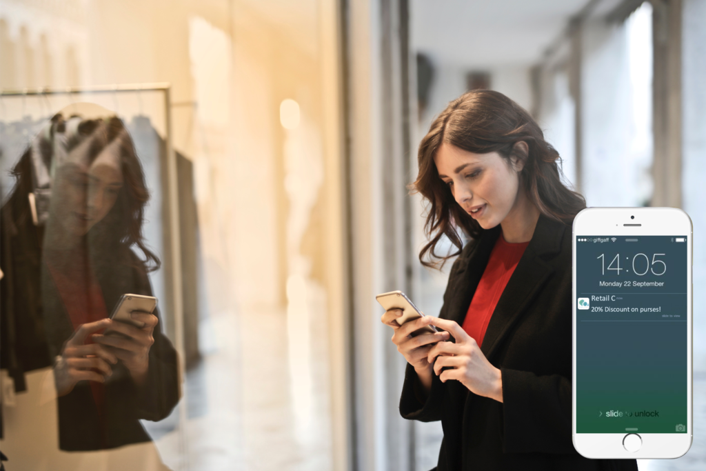A woman is looking a proximity marketing notification that says 20% discount on purses, outside of a store