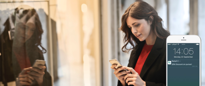 A woman is looking a proximity marketing notification that says 20% discount on purses, outside of a store